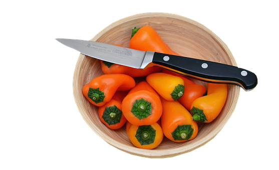 A Bowl Of Orange Peppers And A Knife