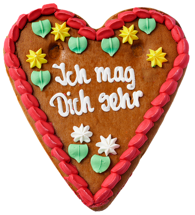 A Gingerbread Heart With White Text And Green And Yellow Flowers