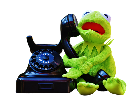A Green Frog Puppet Sitting Next To A Black Telephone