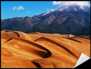 A Sandy Hills With Mountains In The Background With Great Sand Dunes National Park And Preserve In The Background